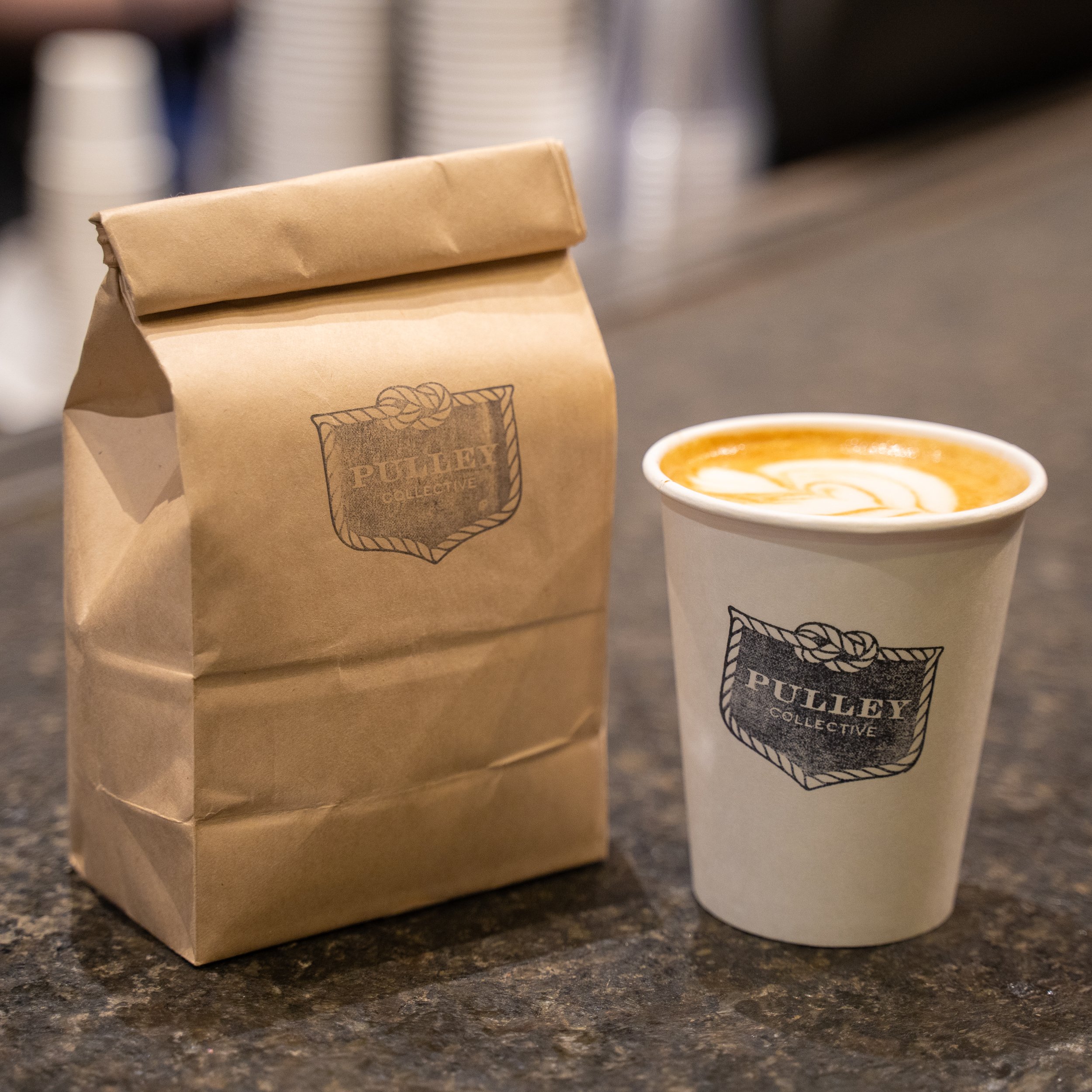 paper bag next to a latte on grey countertop 