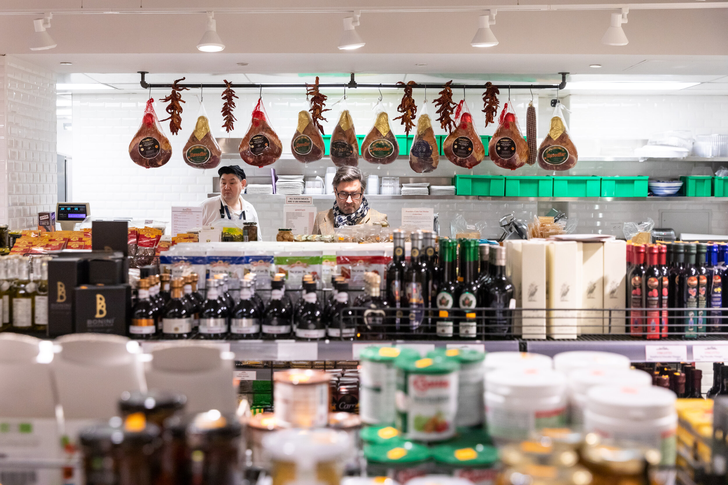 shelves stocked with oils.  hanging, drying meat in the background above the deli counter