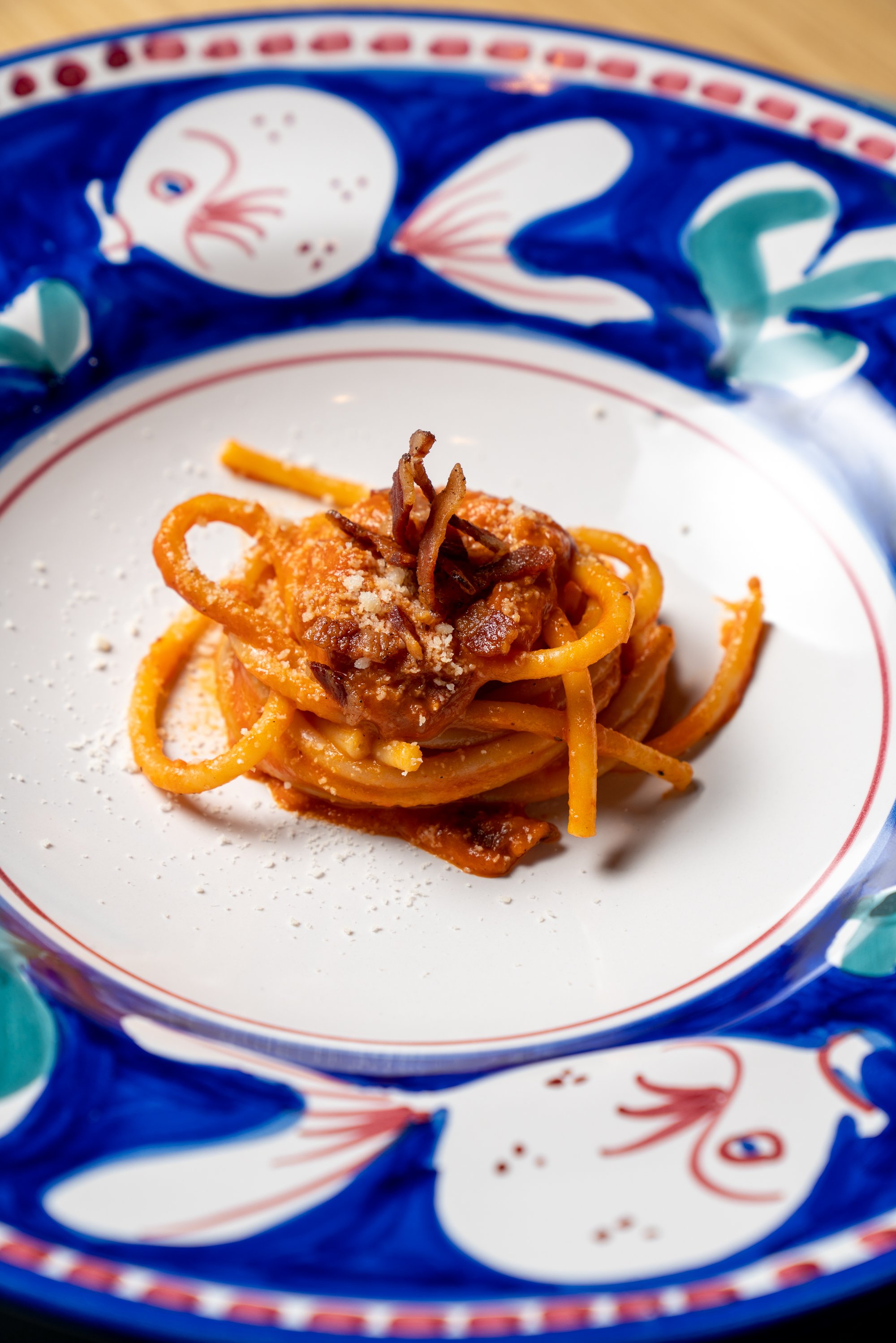 pasta with red sauce, topped with bacon pieces and grated parmesan cheese on blue plate