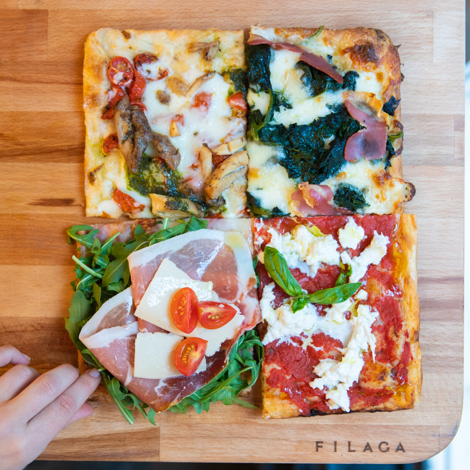 four different square slices of pizza on a wood cutting board 