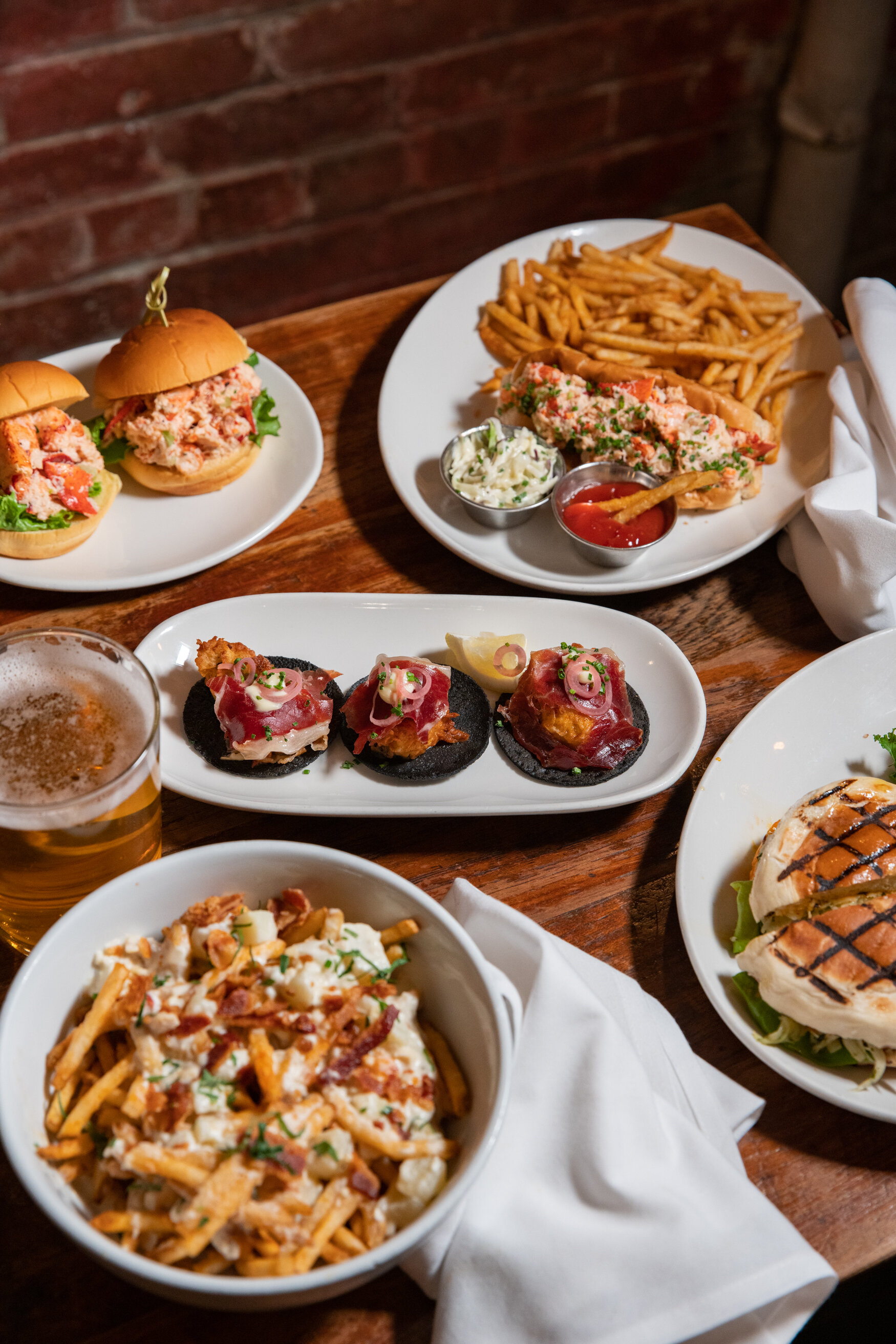 table full with sliders, lobster rolls with french fries, and tartar