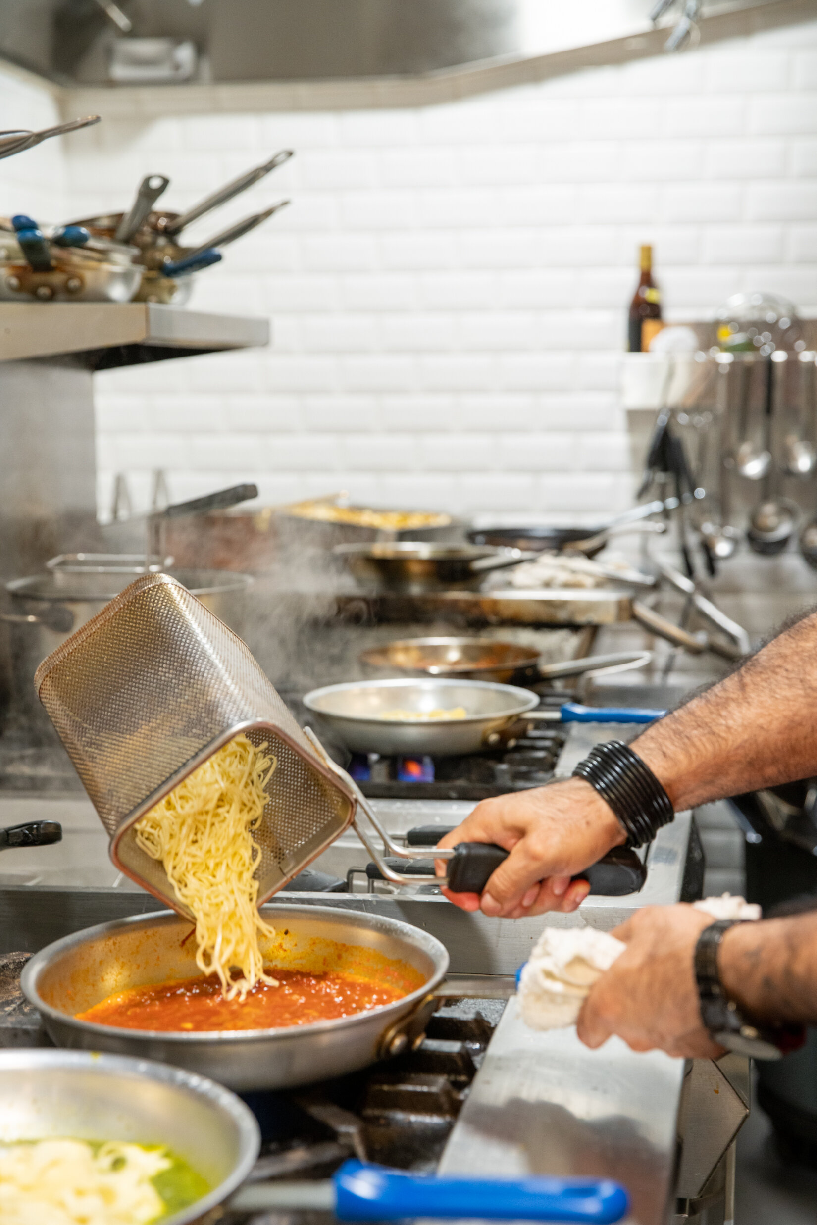 hand pouring cooked pasta into sauce pan filled with tomato sauce on top of a stove