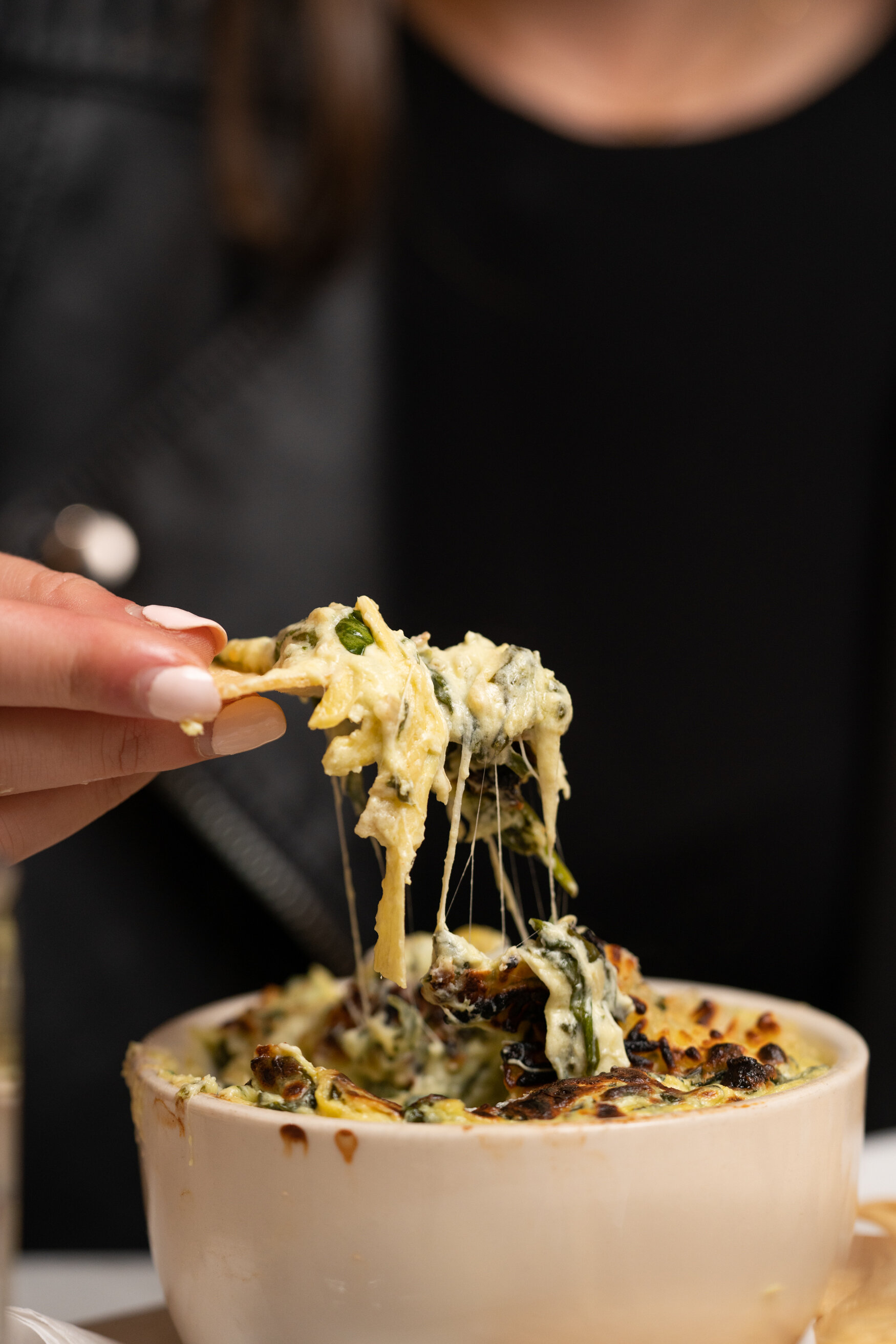 hand holding chip with dip on it.  melted cheese falling 