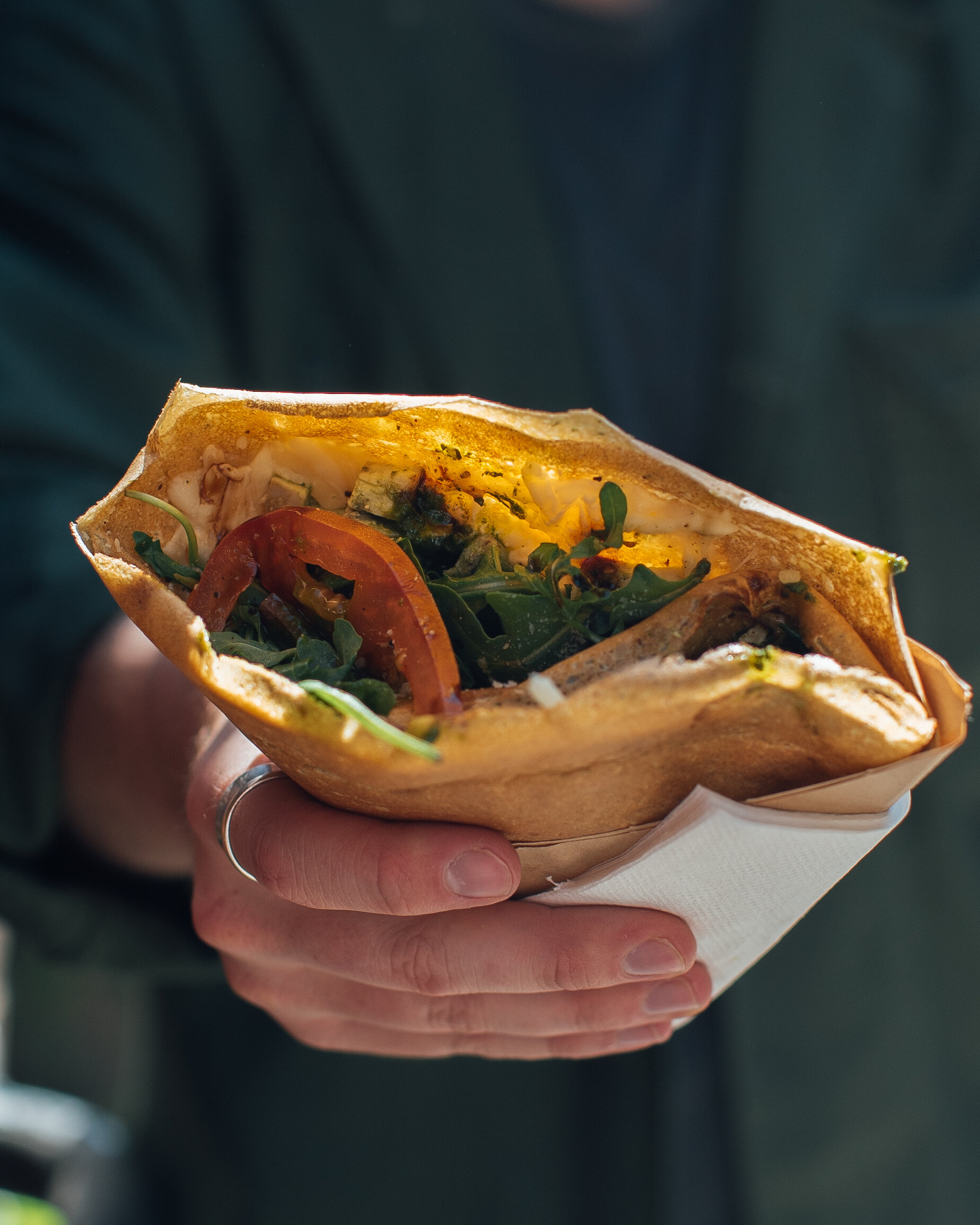 crepe in hand with tomato and arugula poking out