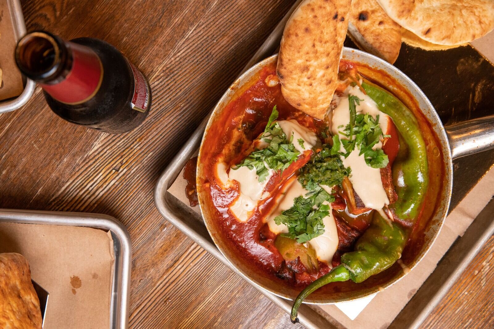 overhead shot of a beer and a pan with fish in a red sauce 